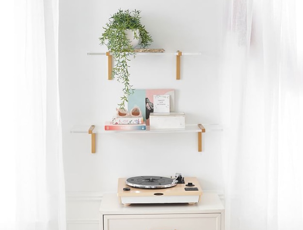 Acrylic and metal floating shelves above a small table with a record player on top of it.