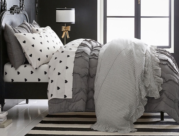 A gray quilt with scalloped ruffles running lengthwise sits on top of a bed.