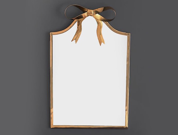 A mirror framed with gold edges features a golden bow on its top.