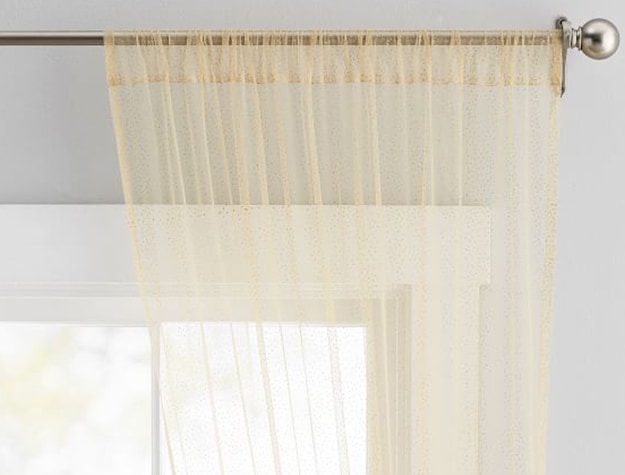 A sheer gold curtain made of tulle hangs in a window.