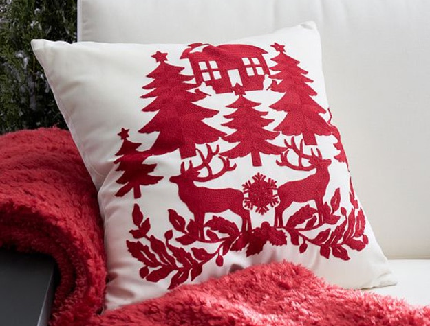 A white pillow with red reindeers and evergreen trees rests on a couch.