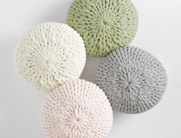 Four chunky knit poufs lay against a white background.