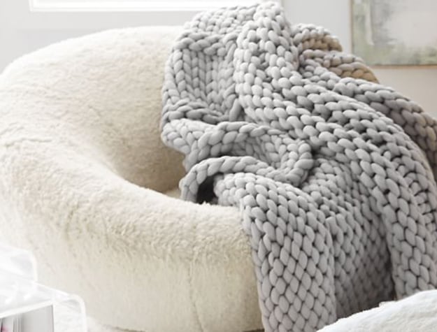 A gray chunky knit blanket lays draped over a fuzzy chair.