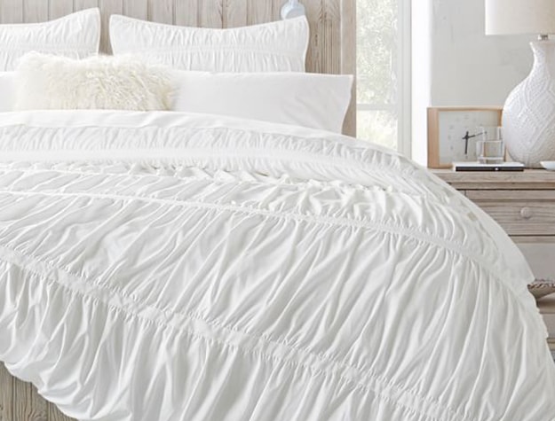 A white bedspread with ruching rests on a bed.