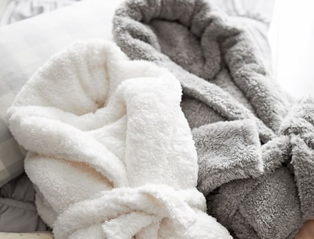 A white sherpa robe lays folded on a couch.