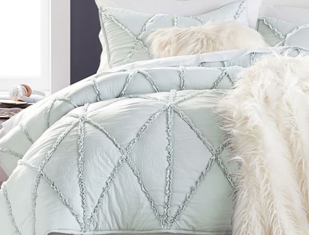 A textured mint bedspread rests on a bed with a cream faux-fur blanket.