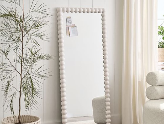 A floor length mirror with a white frame stands in a room.