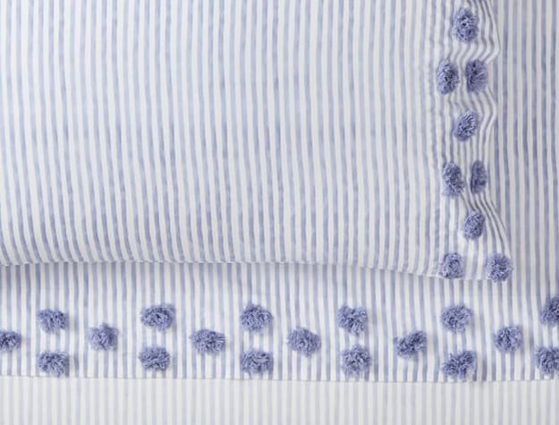 A blue-striped sheet set has small poufed accent balls along the pillow and sheet edges.