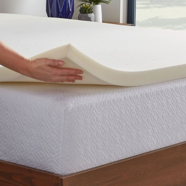  A person putting a memory foam mattress topper on top of their twin XL dorm mattress for extra comfort and padding