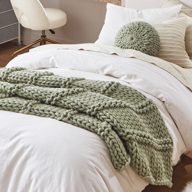 This cozy dorm bed is accented with a sage chunky knit throw blanket and matching chunky knit decorative pillow