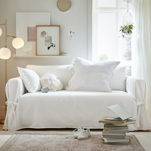 A slipcover sofa couch surrounded by a stack of books and framed art in the background