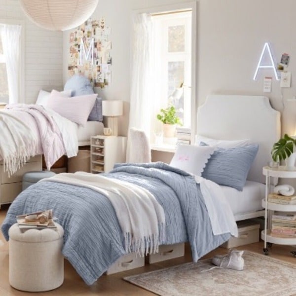 Two beds in a dorm room showing light blue and pink bedding.