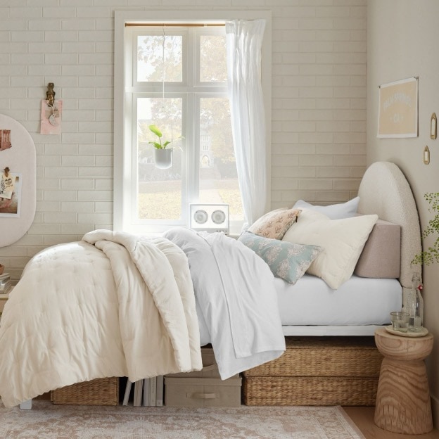 A cozy dorm bedroom defined by a plush comforter, a pile of pillows, and calming decorative accents. 