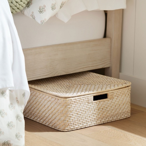 A light wicker basket-style underbed storage bin peeks out from the bed