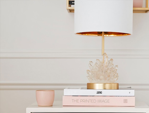 White and gold Geode Burst table lamp on top of a stack of books on a counter next to a pink cup.