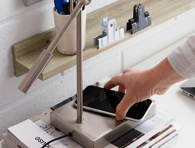 Hand placing cell phone to charge on Ridge PB Charge LED Task Lamp on a stack of magazines.