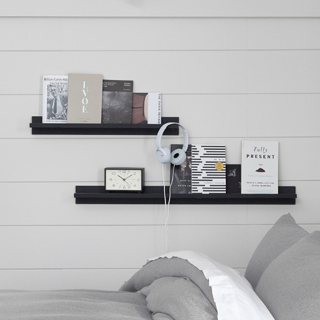 Two black no-nails shelving ledges hold a clock, books, and a pair of headphones, and are conveniently located above the dorm bed for extra storage space